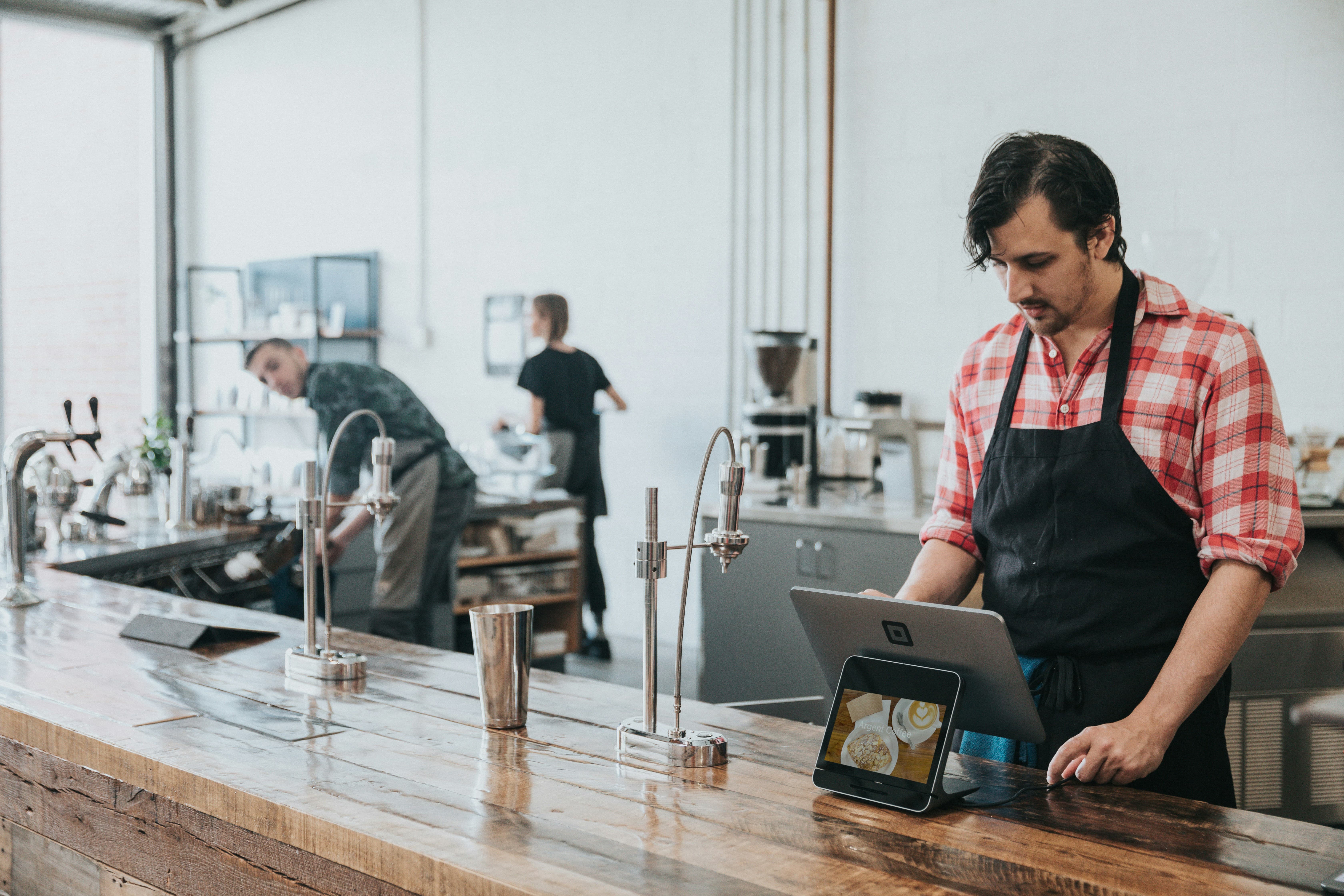 Encargado de cafetería revisando el punto de venta de OnixSnap en una tablet sobre la barra, con el equipo trabajando de fondo